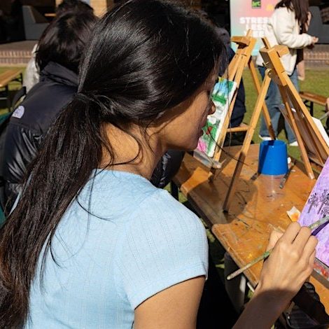 Students painting canvasses on easels in an outdoor setting. 