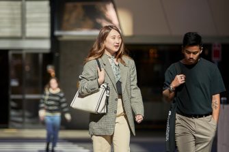 Female in green jacket and male in black t-shirt, law students, walking together behind the law building.  Shadows and light on buildinf exterior.