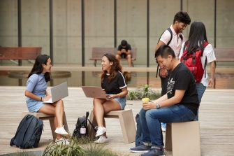Students sitting and standing with laptops at outdoor courtyard
