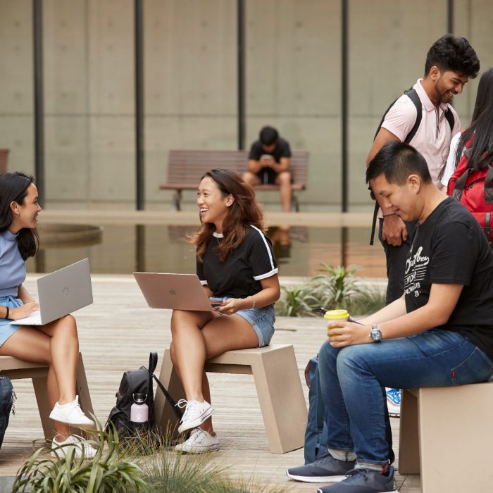 Students sitting and standing with laptops at outdoor courtyard