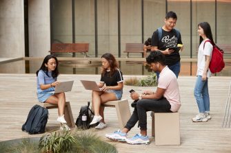 Students sitting and standing with laptops at outdoor courtyard