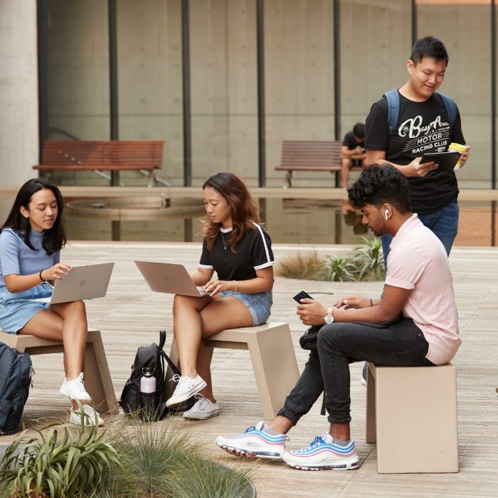 Students sitting and standing with laptops at outdoor courtyard