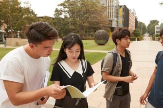 Students with backpacks, headphones, notebooks walking on campus mall