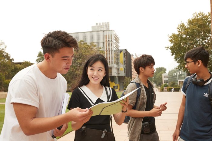 Students with backpacks, headphones, notebooks walking on campus mall