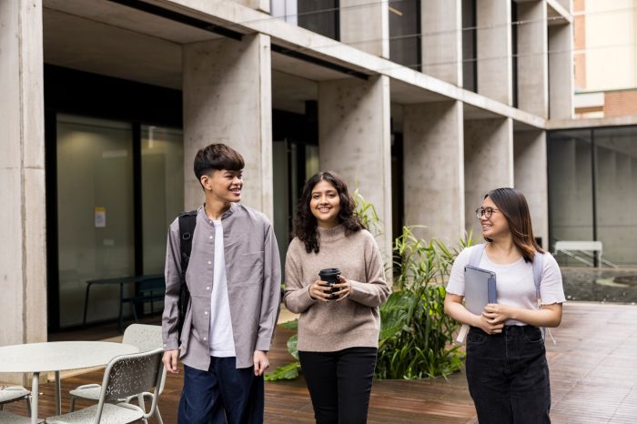 Students walking with backpack, coffee and tablet in courtyard at L5