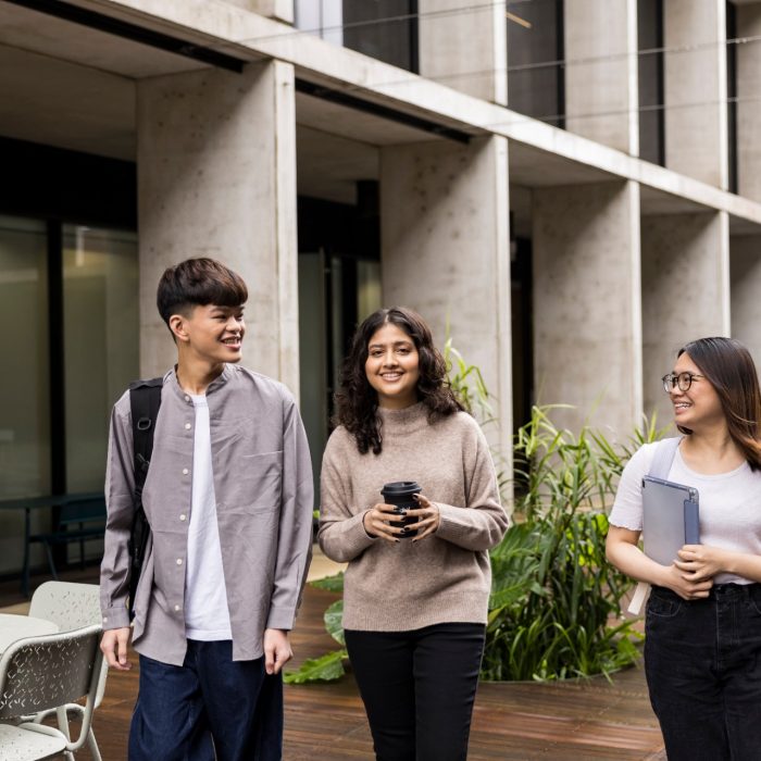 Students walking with backpack, coffee and tablet in courtyard at L5