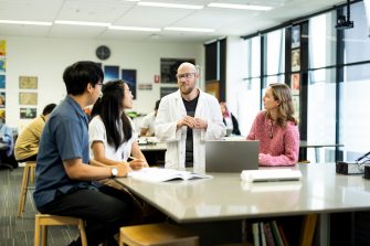 Science Teacher in class discussing with three students