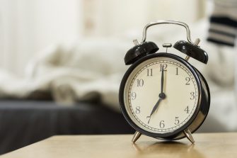 Retro black alarm clock show 7 o'clock in the morning for wake up.Background is a bedroom.