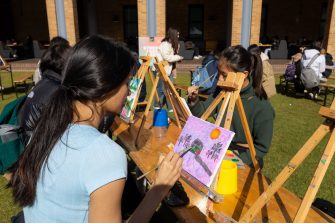 Groups of students sitting at benches and painting on small easels on the Quad Lawn.