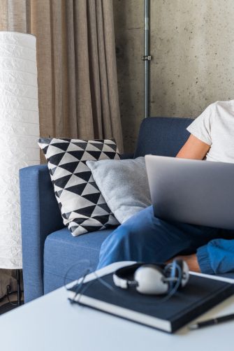 young attractive man sitting on sofa at home working on laptop online, using internet, smiling, happy mood, freelancer, free leisure time, relaxed, modern job lifestyle
