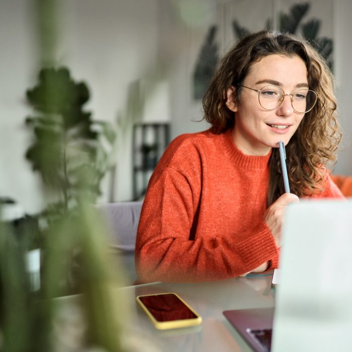 Online learning concept. Young smiling pretty woman student using laptop elearning or remote working at home office using laptop computer watching webinar web course, studying online sitting at table.