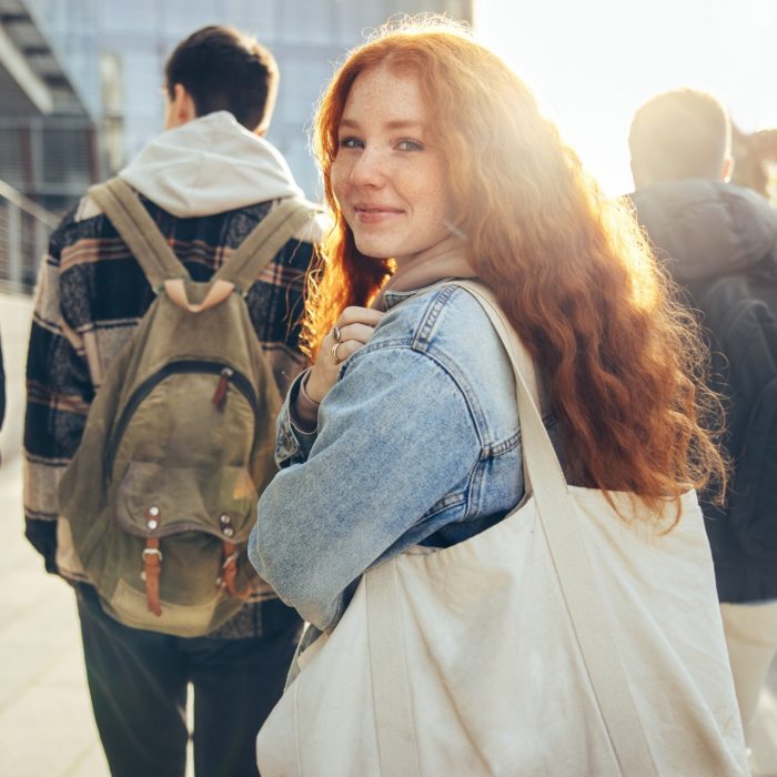 Female student glancing back while going for a class in college. Girl walking with friends going for class in high school.